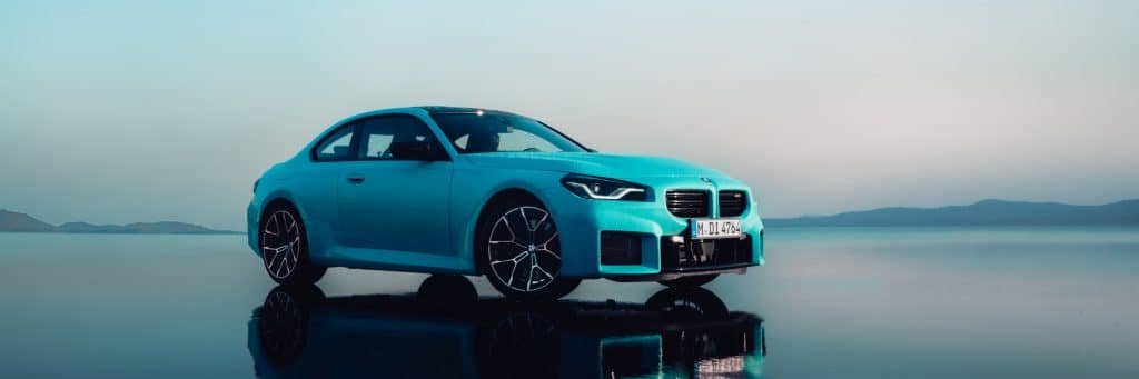 BMW M2 Coupé türkies von schräg vorne auf spiegelnder Oberfläche