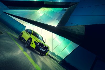 BMW XM gelb auf Straße vor futuristischem Hintergrund