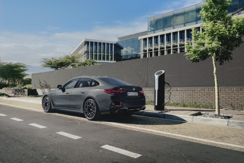 grauer-BMW-i4-vor-futuristischem-Gebäude-an-Ladesäule