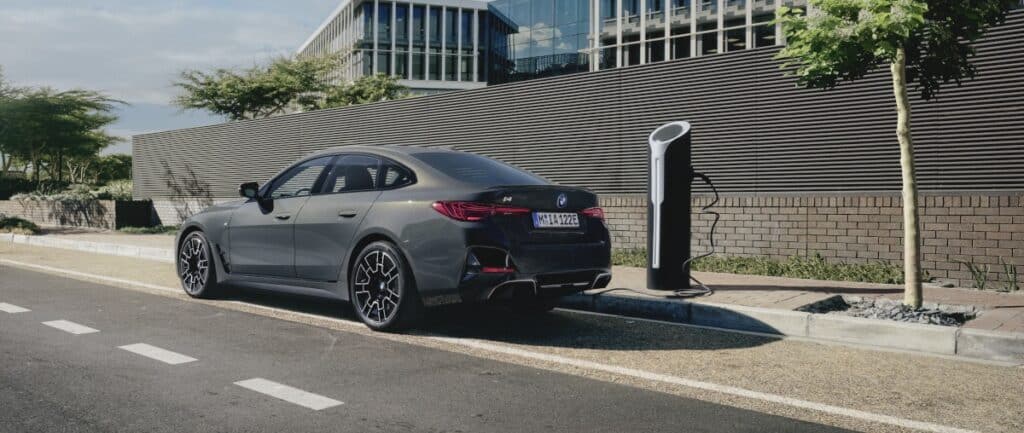 grauer-BMW-i4-vor-futuristischem-Gebäude-an-Ladesäule
