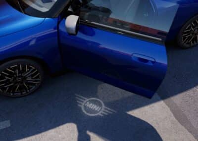 MINI Cooper Electric blau mit geöffneter Tür und MINI Logo auf den Boden profiziert