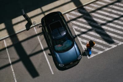 Blick von oben auf MINI Aceman in anthrazit der in einer Parkbox steht, rechts vorne ist eine Frau zu sehen