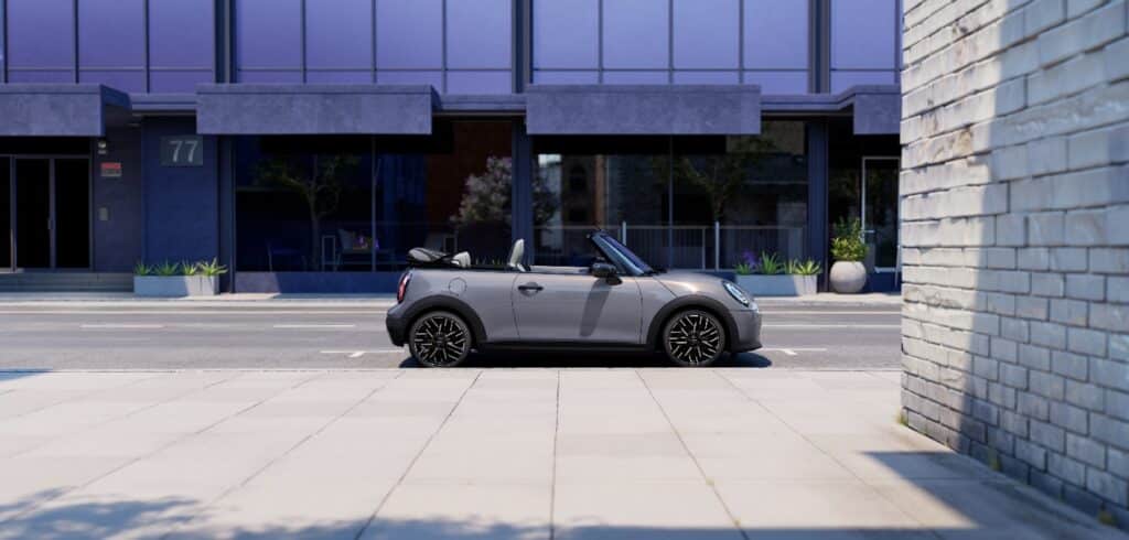 MINI Cooper Cabrio in grau auf einer Straße vor einem modernen Gebäude in Seitenansicht, das Verdeck ist offen