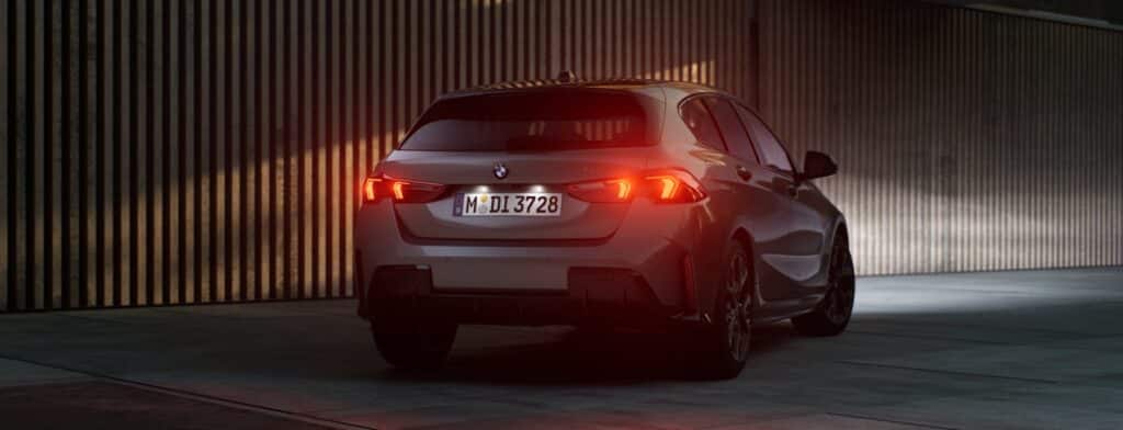 Grauer BMW 1er von hinten in Dunkelheit. Die Heckscheinwerfer leuchten rot.