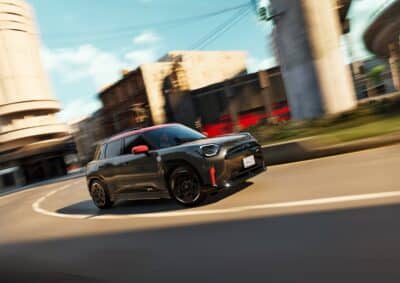 MINI John Cooper Works Aceman in schwarz mit roten Spiegelkappen, Motorhaubenstreifen und Dach auf der Straße - seitliche Ansicht in einer Kurve