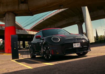 MINI John Cooper Works Electric an Ladesäule in schwarz mit roten Spiegelkappen, Motorhaubenstreifen und Dach