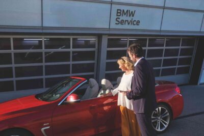 Unterberger BMW Repair Inclusive und BMW Service Inclusive - ein Mann und eine Frau stehen vor einem roten BMW Cabrio vor einer BMW Werkstatt