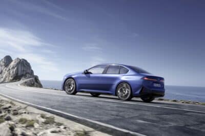 Autohaus Untererger BMW i3 Limousine in blau auf einer Küstenstraße - von schräg hinten