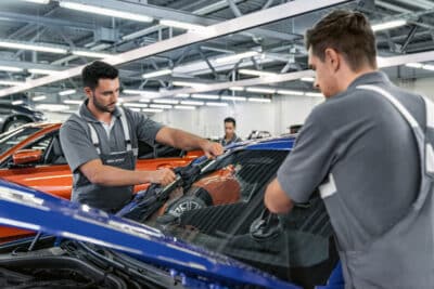 Zwei BMW Mechatroniker tauschen zusammen eine Windschutzscheibe eines Fahrzeuges