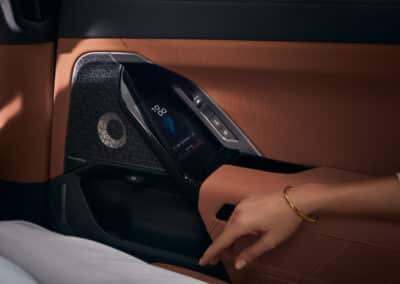 Innenansicht der Türverkleidung mit Touchdisplay der BMW 7er Limousine. Eine Frauenhand liegt auf der Armablage. Hellbraunes Leder