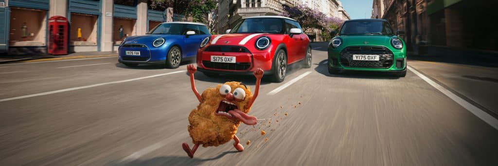 MINI Schnitzeljagd Probefahrtaktion - ein blauer, ein roter und ein grüner MINI fahren hinter einem panisch blickendem Schnitzel hinterher
